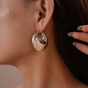 Close-up of geometric textured silver wide hoop earring with woven pattern on earlobe