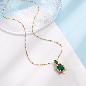 Gold turtle necklace featuring emerald green stones and white zircon on white surface