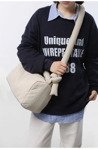 Detail of a beige quilted puffer crossbody bag featuring a unique wide knotted shoulder strap