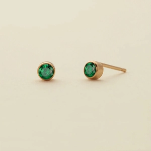 Macro view of round emerald stud earrings in gold bezel setting for women