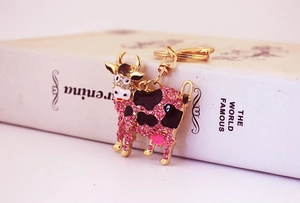 Detail of a gold metal cow keychain featuring pink rhinestones and black enamel accents