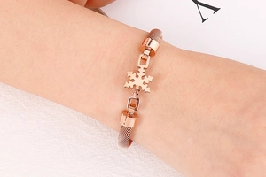 Détail d'un bracelet en maille or rose avec motif flocon de neige porté au poignet