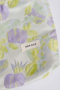 Detail of floral makeup bag featuring H&R BAG woven label and intricate fabric texture
