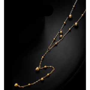 Minimalist gold tassel necklace with polished beads shown on a black background