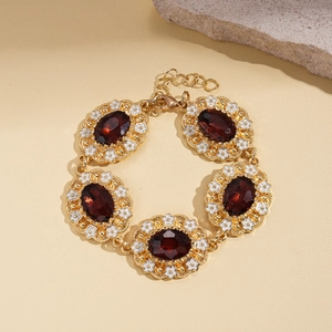 Detailed macro view of vintage gold bracelet with deep red gems and white flower enamel