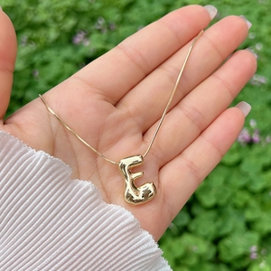 Macro detail of high-shine gold-plated 3D bubble letter E pendant necklace for women