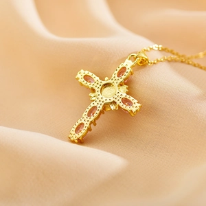 Close-up of gold plated cross pendant with pink zircons on soft pink silk fabric