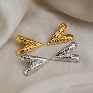 Detailed view of heart-shaped gold and silver earrings with hammered texture on silk