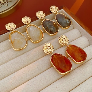 Detail showing irregular gold textured earrings with resin pendants in velvet box