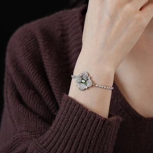 Close-up of silver-tone bracelet with emerald-cut green gemstone and filigree details