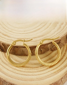 Close-up of golden hoop earrings with radial texture on a rustic wooden background