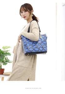 Detailed close-up of blue snakeskin pattern tote bag with black leather base and gold rivets