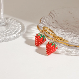 Golden stainless steel hoop earrings with red enamel strawberry charms on textured glass