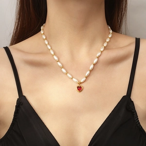 Elegant gold necklace with red heart crystal pendant and white faux pearls on model