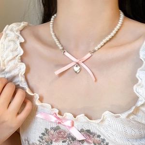 Macro detail of pearl necklace featuring a pink ribbon bow and silver heart pendant