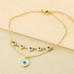 Détail d'un bracelet doré à double chaîne orné de charmes en forme d'œil grec bleu