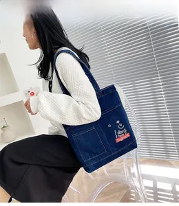 Dettaglio della borsa tote in denim blu scuro con ricamo bianco e tasche laterali