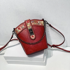 Detail of red bucket bag featuring intricate embroidery, metal chain and leather strap