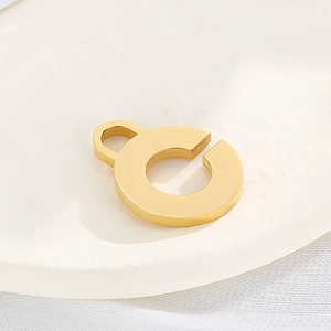Golden round hollow letter G stainless steel pendant charm on white display tray