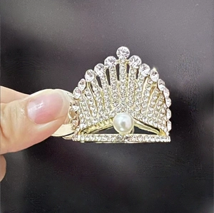 Detail of gold crown hair clip featuring sparkling rhinestones and a white central pearl