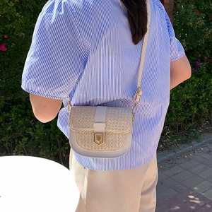 Retro cream-colored woven saddle bag with gold buckle shown on shoulder in a garden