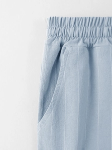 Macro detail of elastic drawstring waist and side pockets on light blue striped linen pants