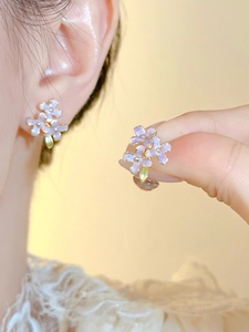 Detailed macro shot of lavender floral earrings with golden center and green leaf charms