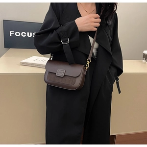 Detail of dark brown leather crossbody bag styled on a black coat with focus signage