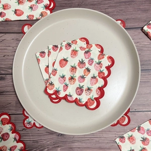 Cocktail napkins featuring red strawberry print and scalloped edges on a ceramic plate