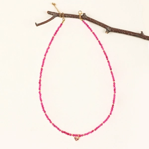 Detail of bohemian magenta stone beaded necklace with a heart pendant on a branch