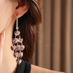 Macro detail of long silver fringe earrings with pink heart crystals on model