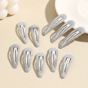 Detail of ten silver glitter teardrop snap hair clips on a textured beige surface
