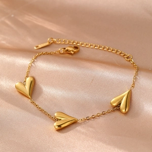 Detail of three polished gold heart charms on a stainless steel bracelet with lobster clasp