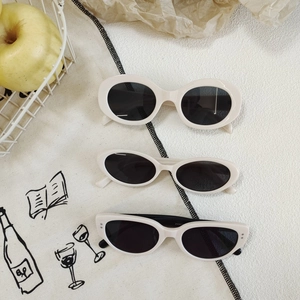 Three pairs of cream-white vintage cat-eye sunglasses with dark lenses on a retro tablecloth