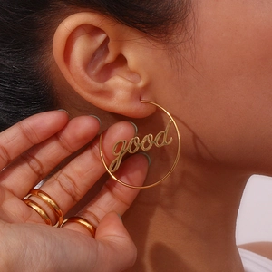 Close-up of a gold hoop earring with 'good' lettering shown on a female model