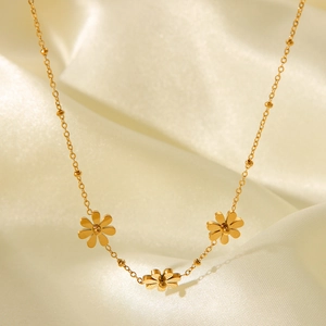 Detail of three golden daisy pendants on a delicate bead chain over silk fabric