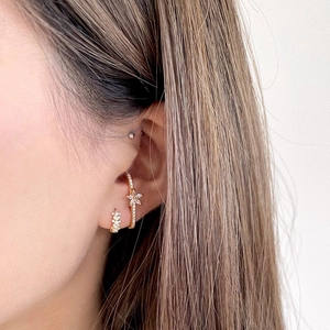Detail of gold flower ear cuffs and huggie earrings with cubic zirconia on female model