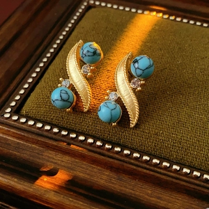 Macro shot of vintage style S-shaped gold earrings with turquoise beads and rhinestones