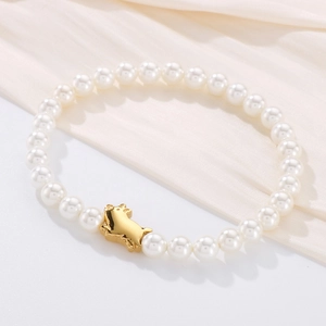 Close-up of pearl bracelet with gold pig charm on elegant silk fabric background