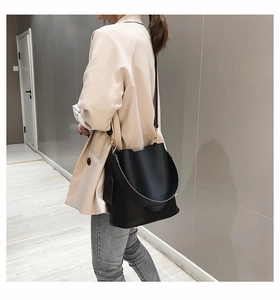 Détail du sac seau en cuir noir avec large bandoulière et boucles dorées sur le mannequin