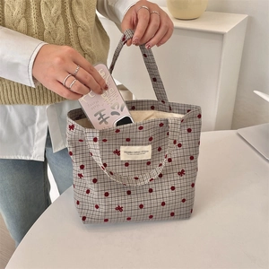 Détail montrant le rangement d'un smartphone dans le sac à lunch en toile à carreaux