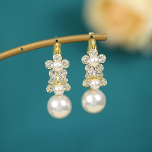 Close-up of elegant gold flower petal earrings with hanging pearls and zircon accents