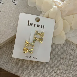 Set of four shiny gold bow hair clips displayed on a card with a vintage background