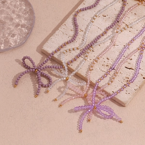 Close-up of beaded necklaces with colorful crystal beads and a bow pendant on beige stone