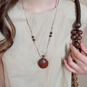 Detail of wooden gourd pendant necklace with wax rope and beads on a linen shirt