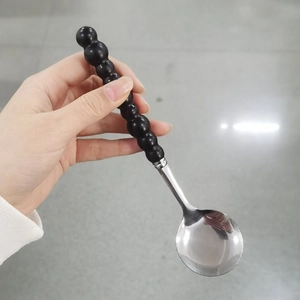 Close-up of stainless steel spoon with black pearl beaded handle held by hand