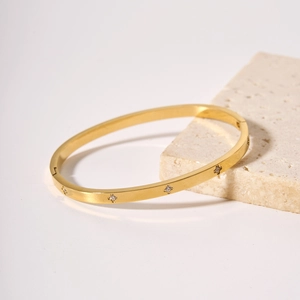 Bracciale in acciaio inossidabile dorato con zirconi a stella su sfondo di pietra