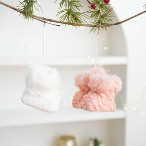 Detail of plush white and pink Christmas boot ornaments hanging on a pine branch