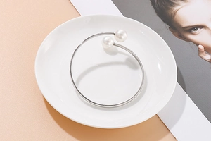 Detail of silver open cuff bracelet featuring dual white pearls on a minimalist white plate