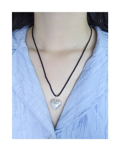 Detail of silver heart pendant on a black cord necklace worn on a female model